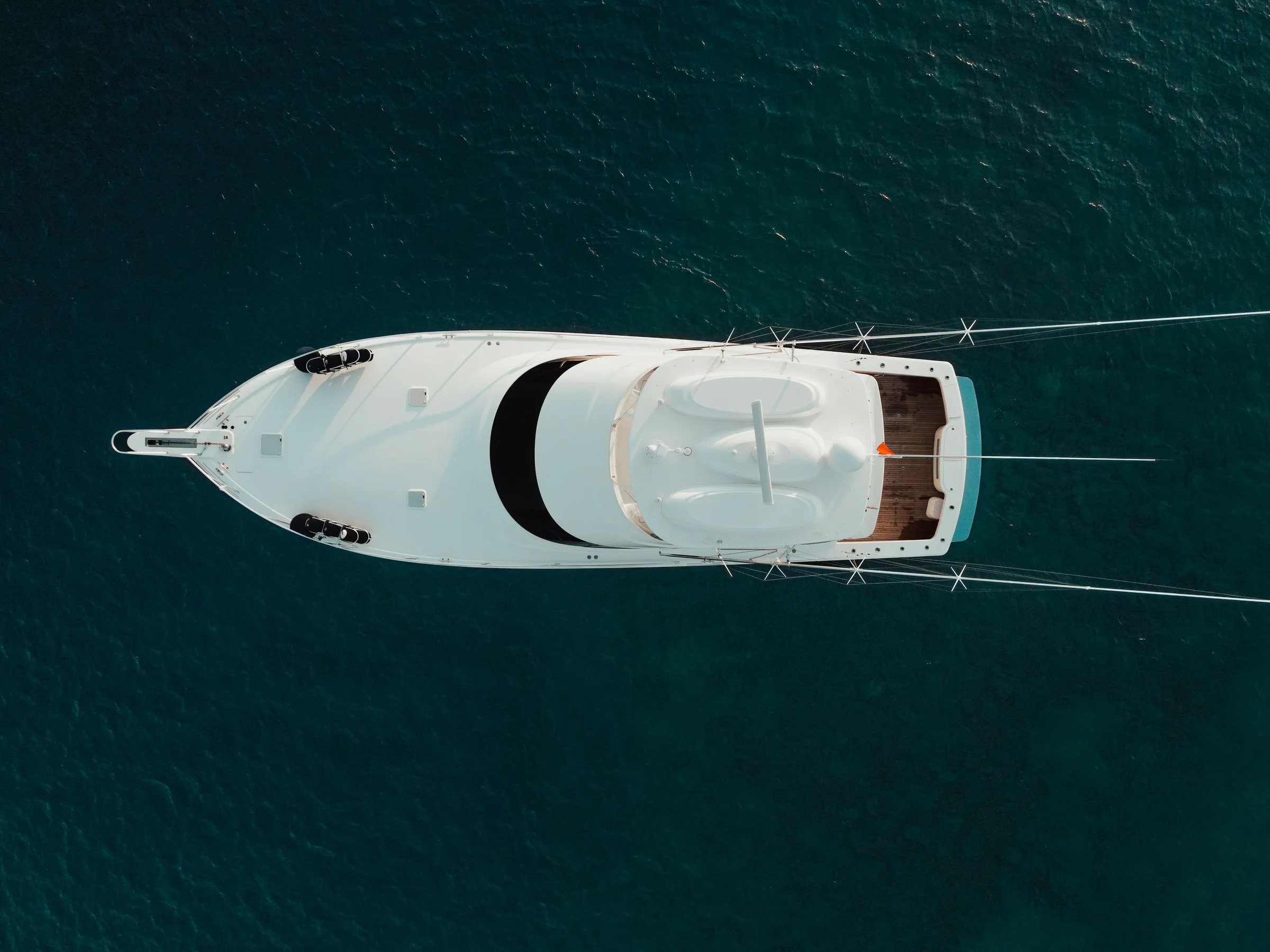 A sportfishing yacht from directly above, outriggers out, on deep blue water